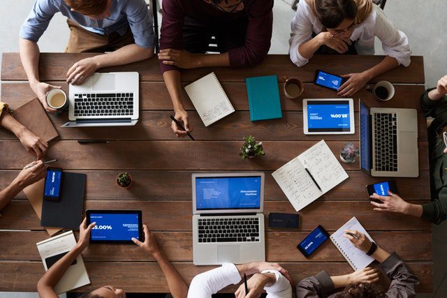 top view of employees board table filled with laptops, tablets and notes