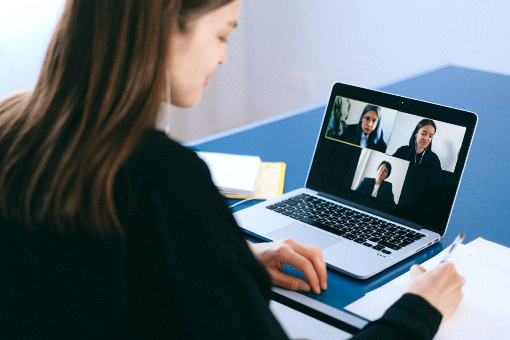 Young female employee writing notes diary during virtual collaboration with other teammates.