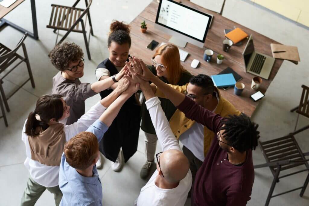 Different diversity employees joining hands for hifigh in office.