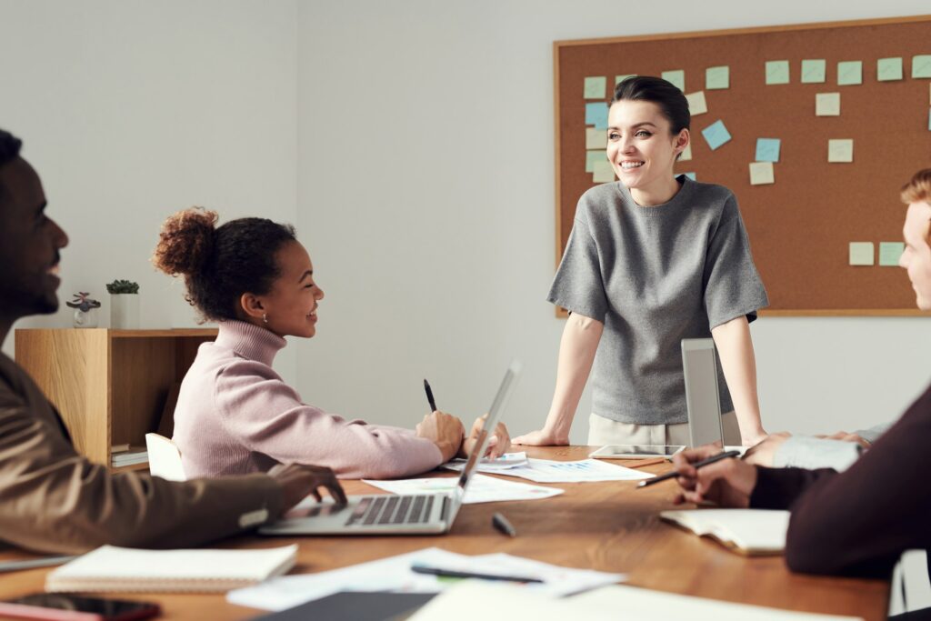 a woman standing near the desk and three other people sitting and talking to each other