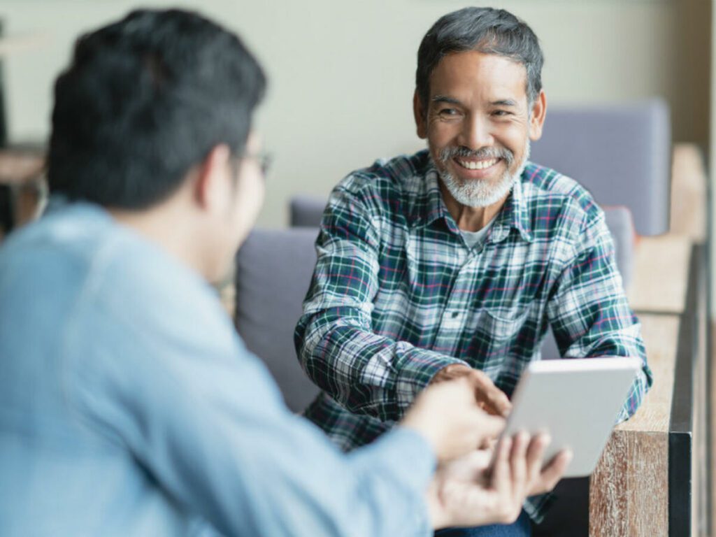 two man laughing and talking to each other while sharing tablet screen