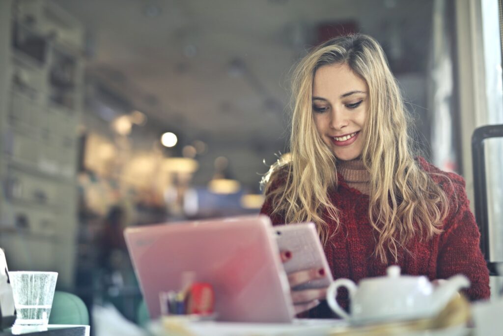 Happy Female business woman dressed in red top using mobile from office canteen.