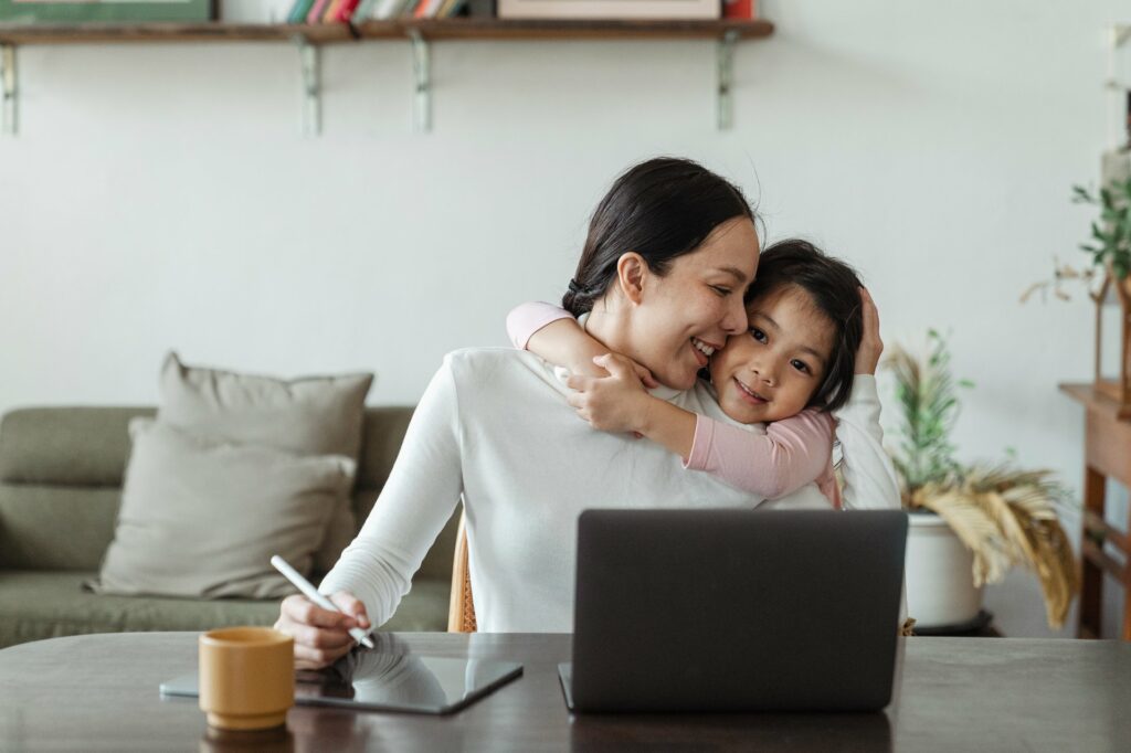 a woman hugging her daughter and working on the laptop