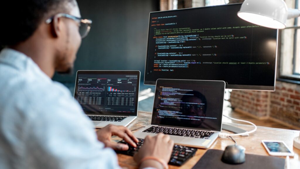 employee looking at the code on two laptops and one monitor 