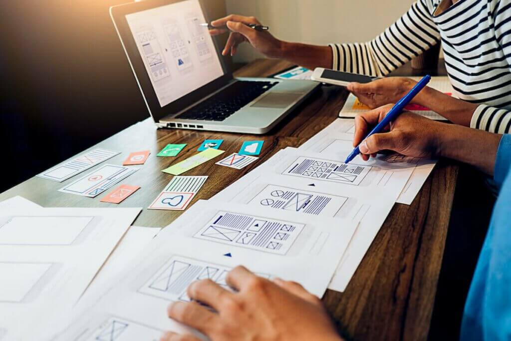 UX team working app layouts sketches on white paper and from laptop