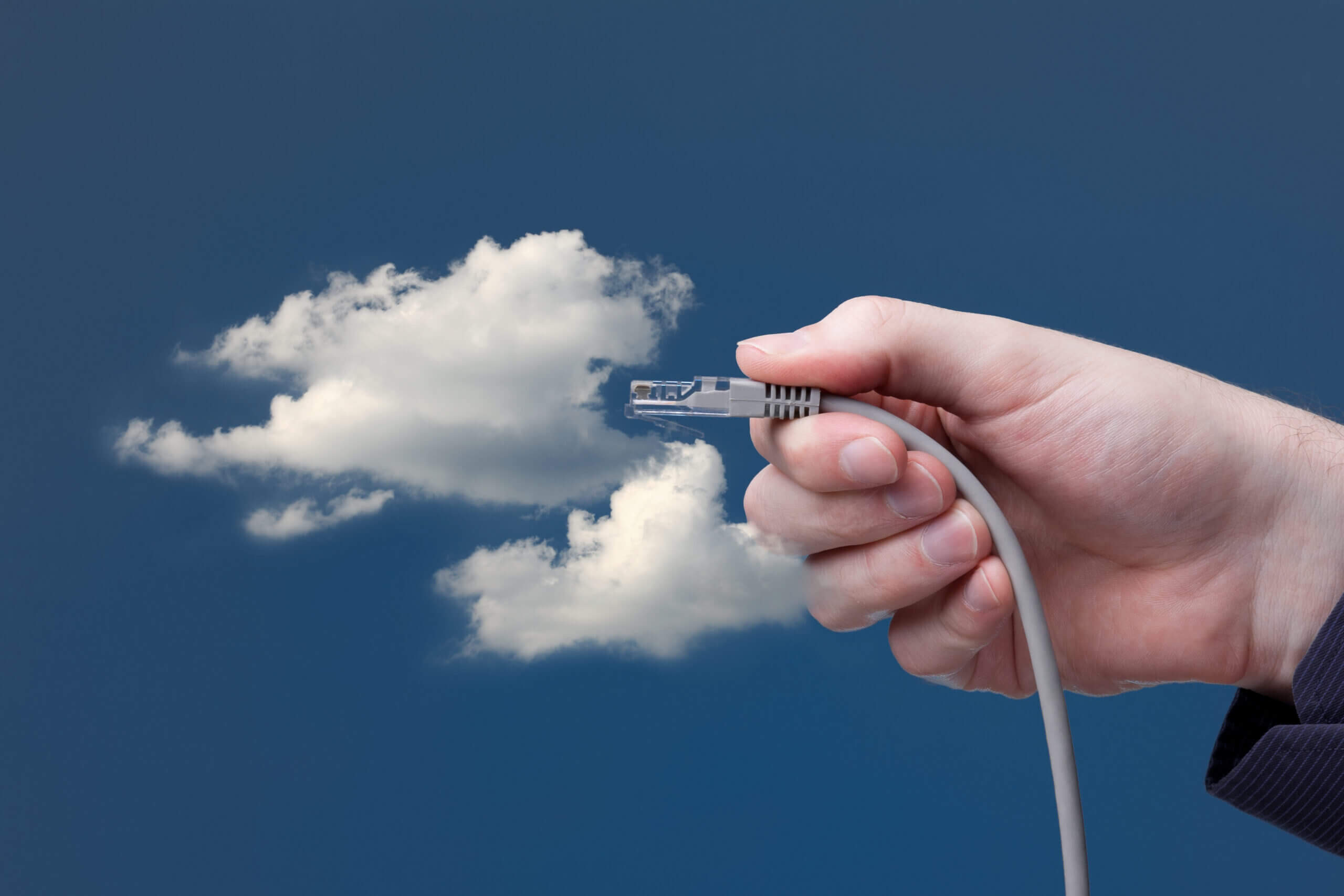 employee hand holding cable and connecting to clouds in sky.