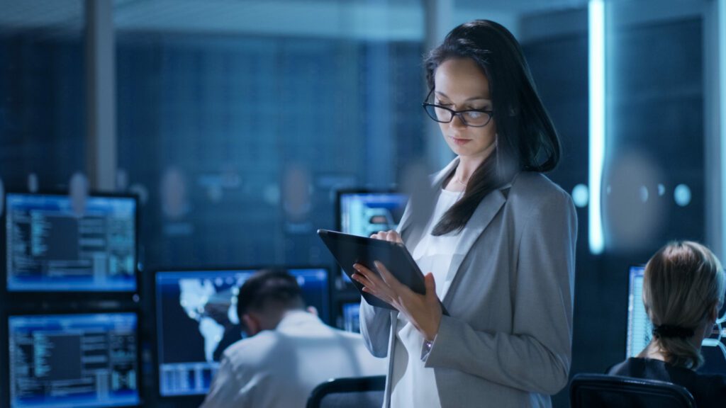 A women in the office working on tablet. two people in the background on the computer