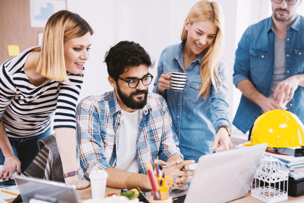 Group of IT employees sharing laptop screen while drinking coffee.