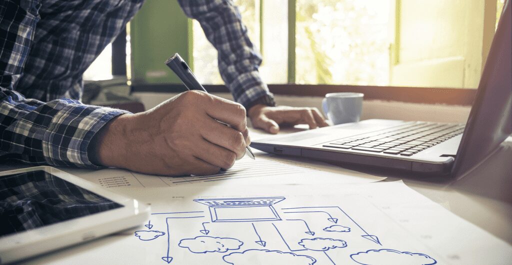 Cloud engineer sketching cost optimisation process on white paper while working with laptop