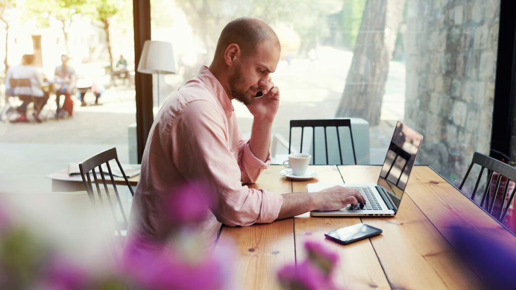 IT Business man talking on mobile working with laptop from cafe