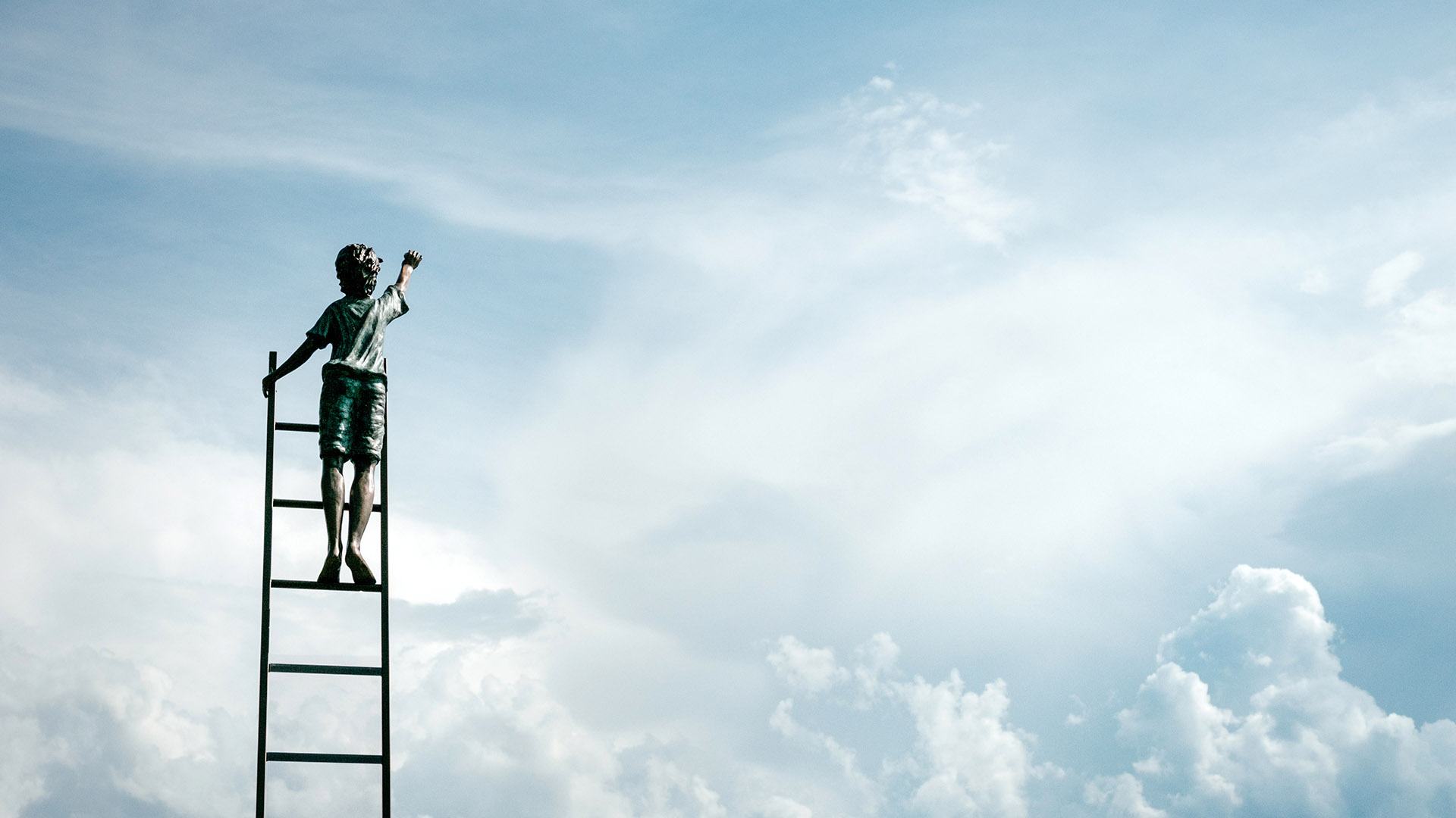 young child standing at top of ladder raising one hand towards sky.