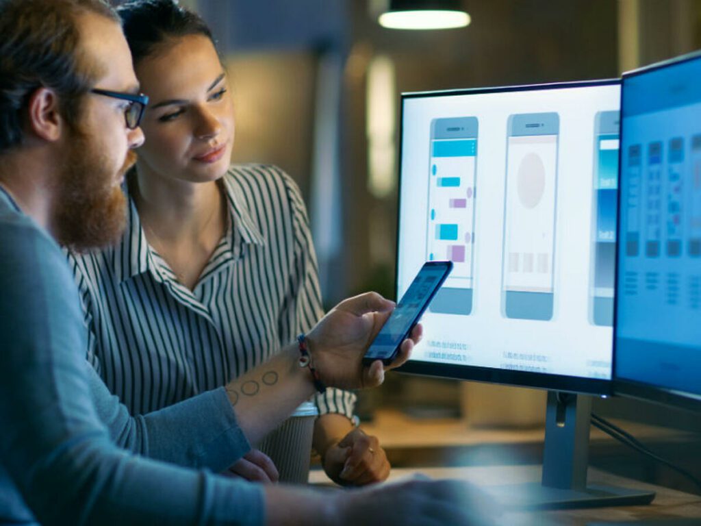 man and woman looking at computer screen and mobile screen analysing low code no code software development