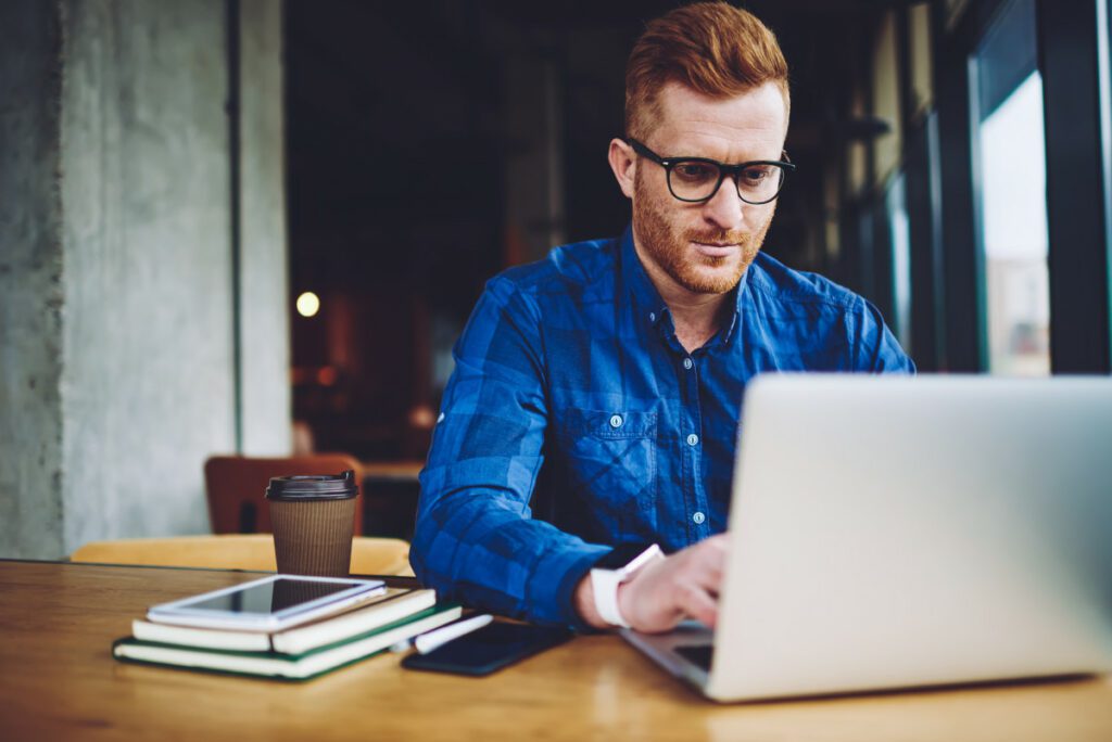 IT engineer working on AI platforms with laptop and his work desk having coffee cup, books and mobile on it.