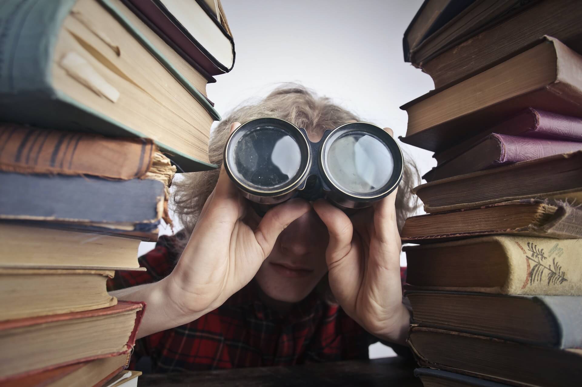 man with binoculars between books