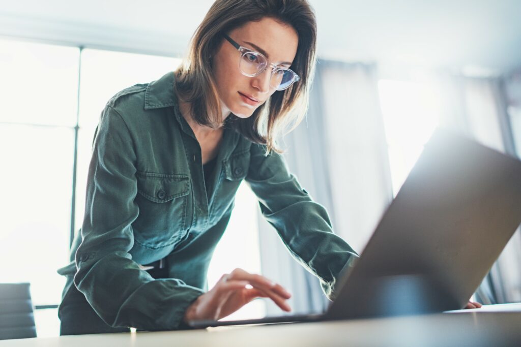 Young female artificial intelligence engineer working with laptop from office desk on XAI algorithms.