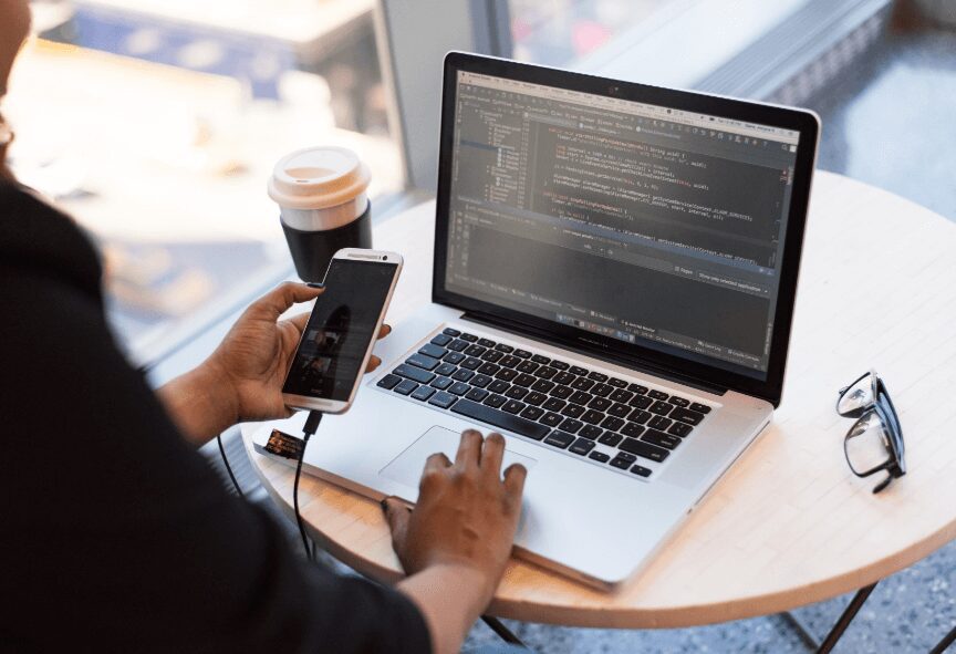 employee working on coding in laptop while using mobile.