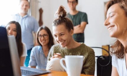 group of smiling employees watching laptop screen