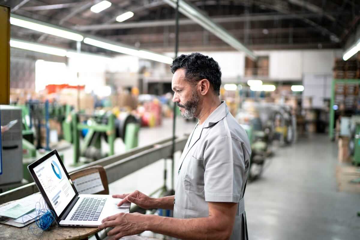 A man standing and working on computer to optimize supply chain integration in factory