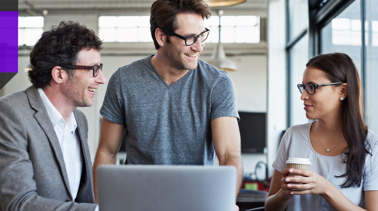 Two IT men smiling while chatting with young female IT employee drinking coffee and working together
