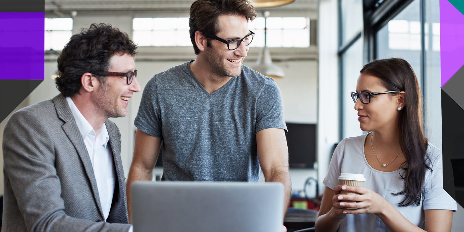 Two IT men smiling while chatting with young female IT employee drinking coffee and working together