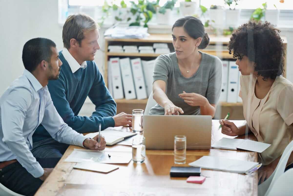 Four employees discussing task automation. Notebooks and laptop on the table.