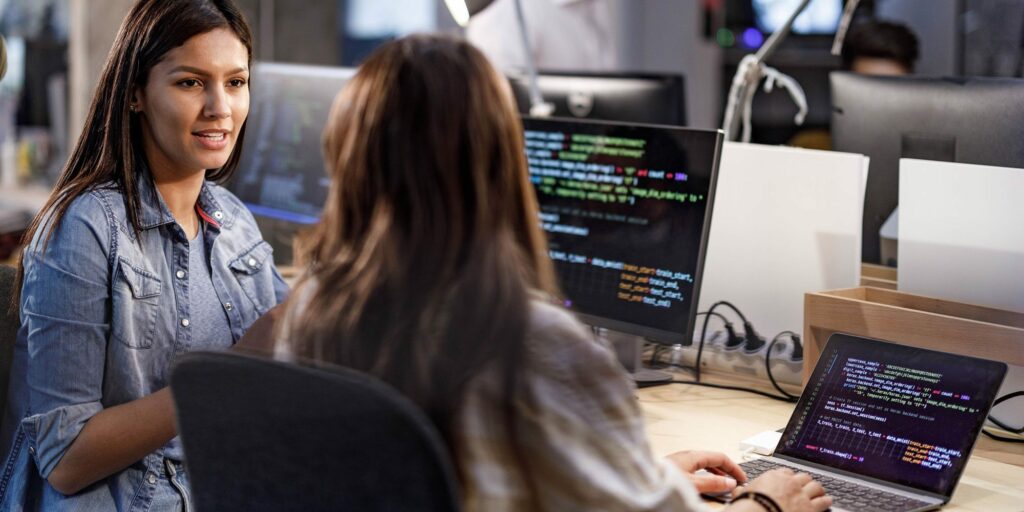 Two women sitting at work desk and discussing microservices web apps