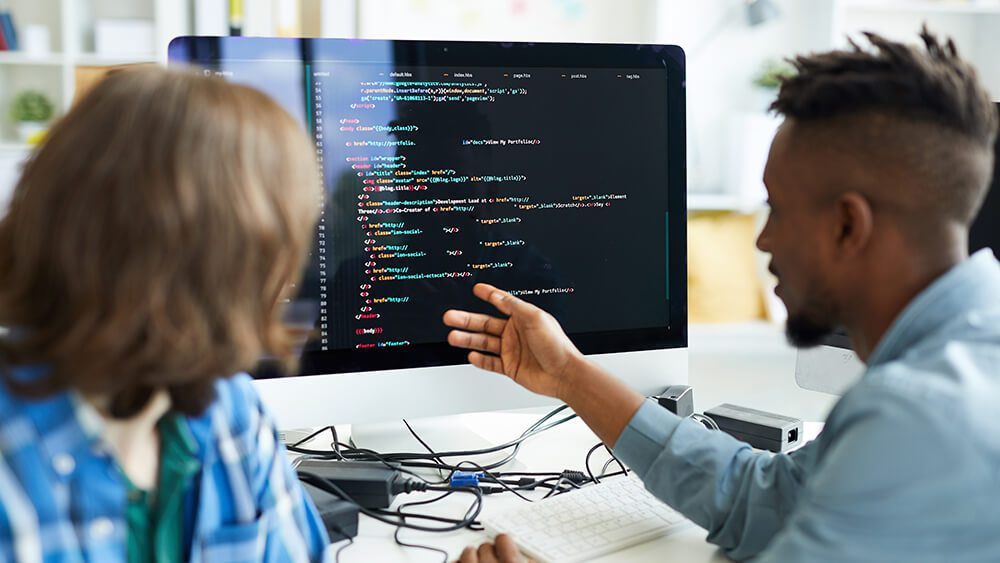 A woman and a man sitting at work desk and discussing microservices web apps